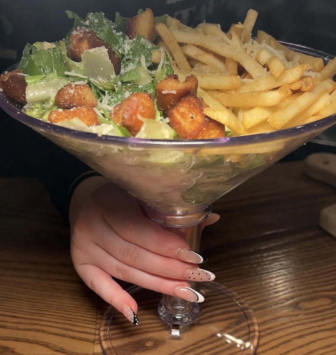 Camera photo of high-quality of Ceaser Salad and French Fries, neatly placed inside of a large martini glass.